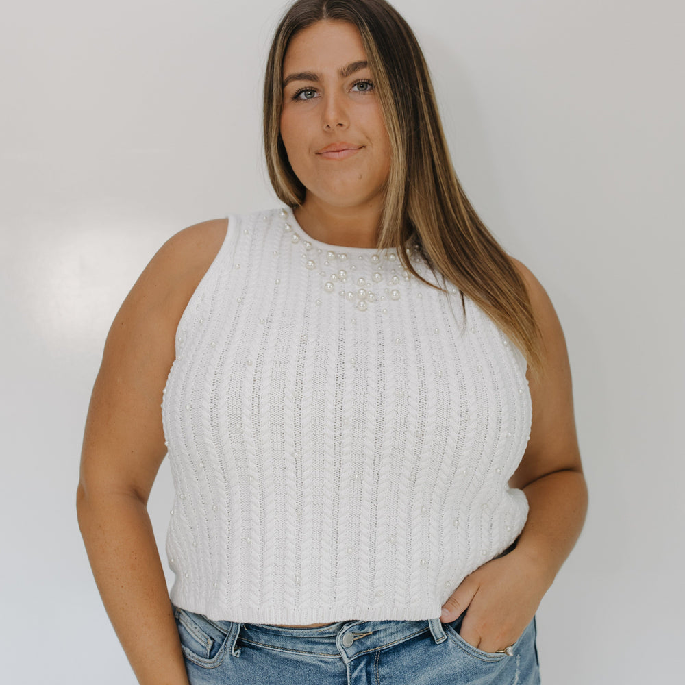 Woman wearing a white sleeveless top and blue jeans against a plain background