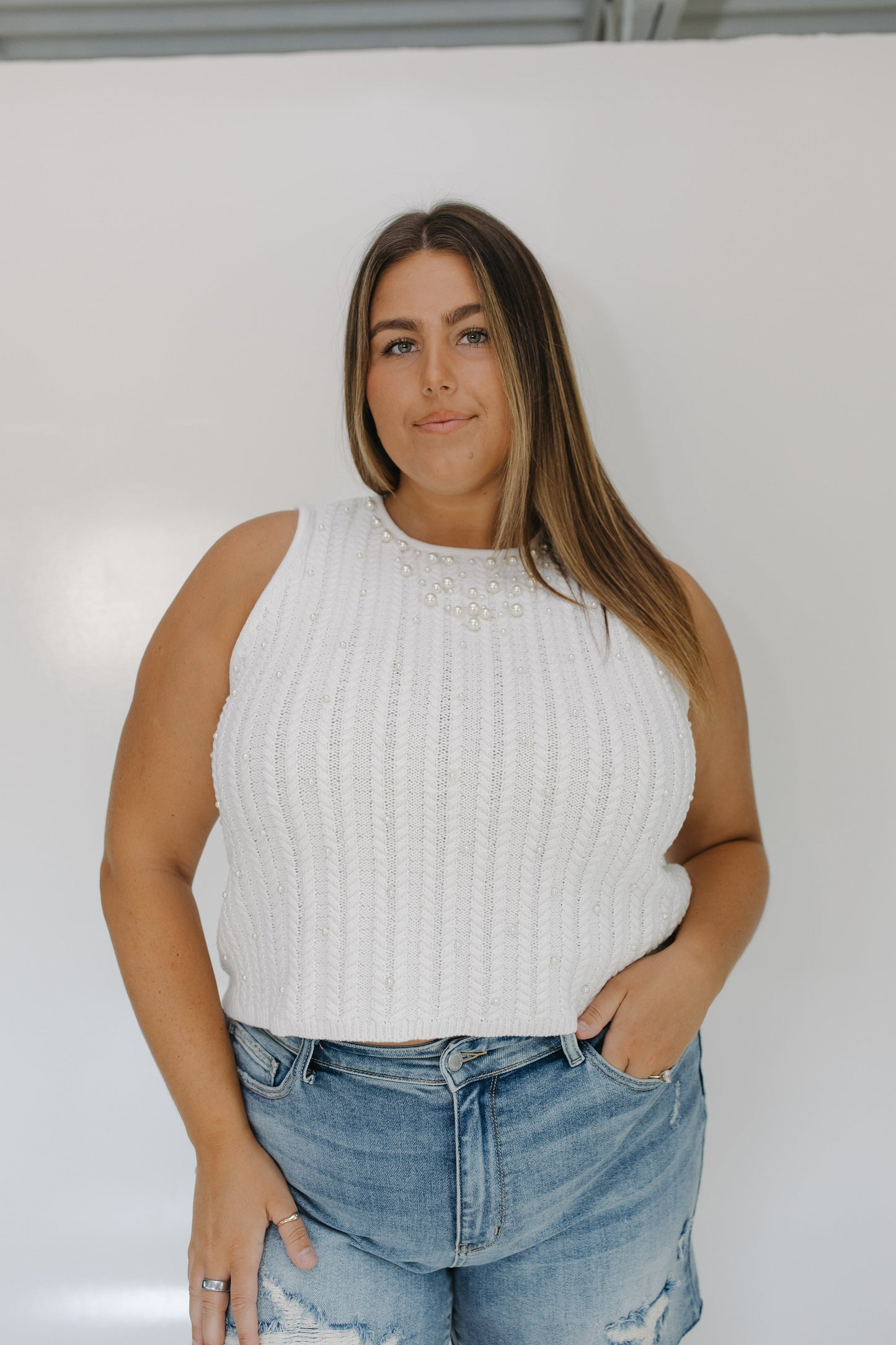 Woman wearing a white sleeveless top and blue jeans against a plain background