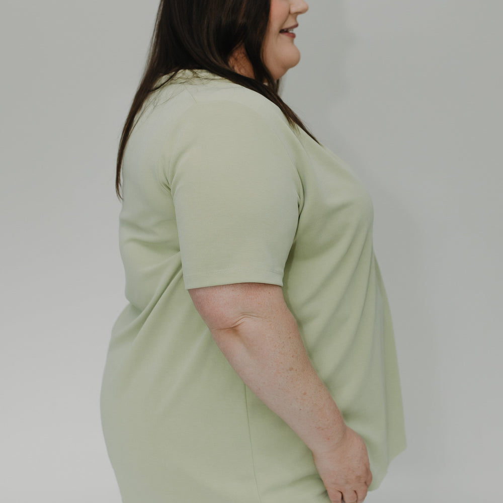 Woman wearing a light green t-shirt and white shorts against a plain background