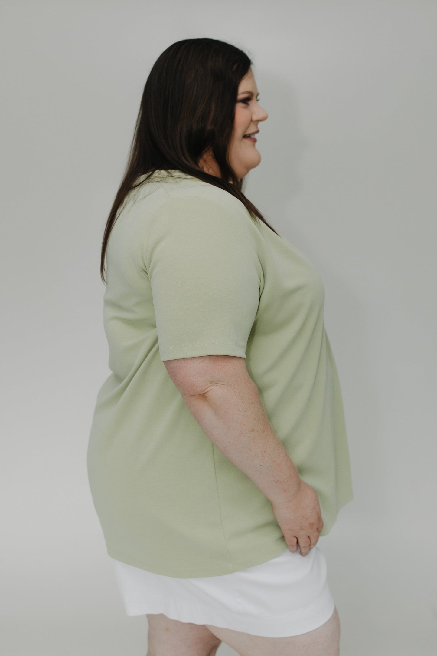 Woman wearing a light green t-shirt and white shorts against a plain background