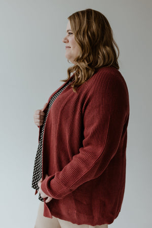 A woman with wavy brown hair is wearing the Yesta KNIT OPEN CARDIGAN IN CRANBERRY over a polka dot top, standing sideways against a plain background.