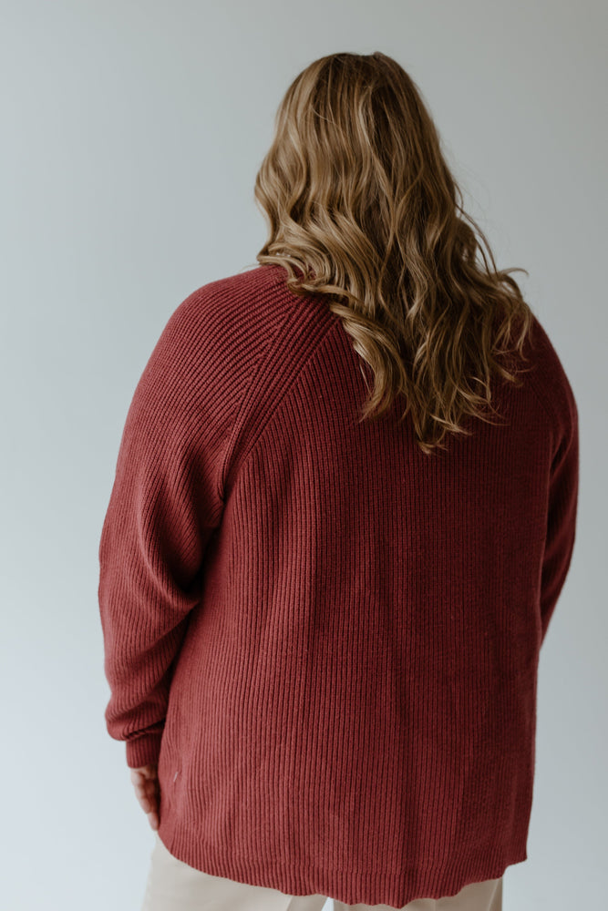 A person with wavy, long brown hair is wearing the KNIT OPEN CARDIGAN IN CRANBERRY by Yesta, standing with their back to the camera against a plain background.