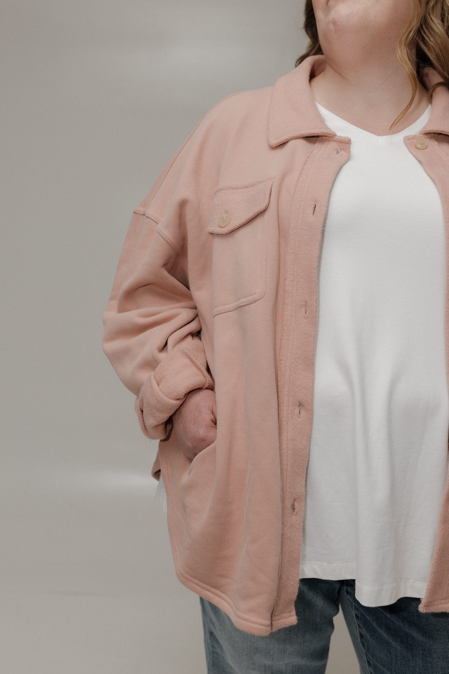 Person wearing a light pink jacket over a white shirt with a neutral background