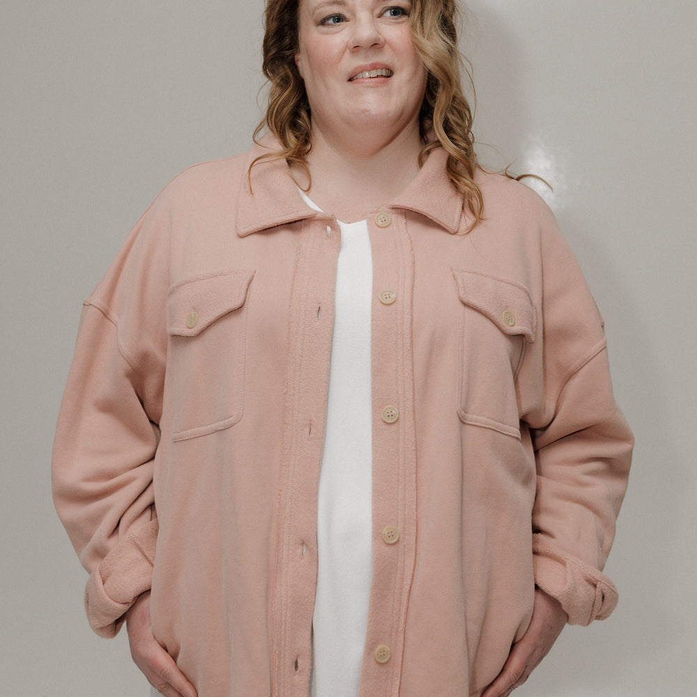 Person wearing a pink jacket over a white shirt with a plain background
