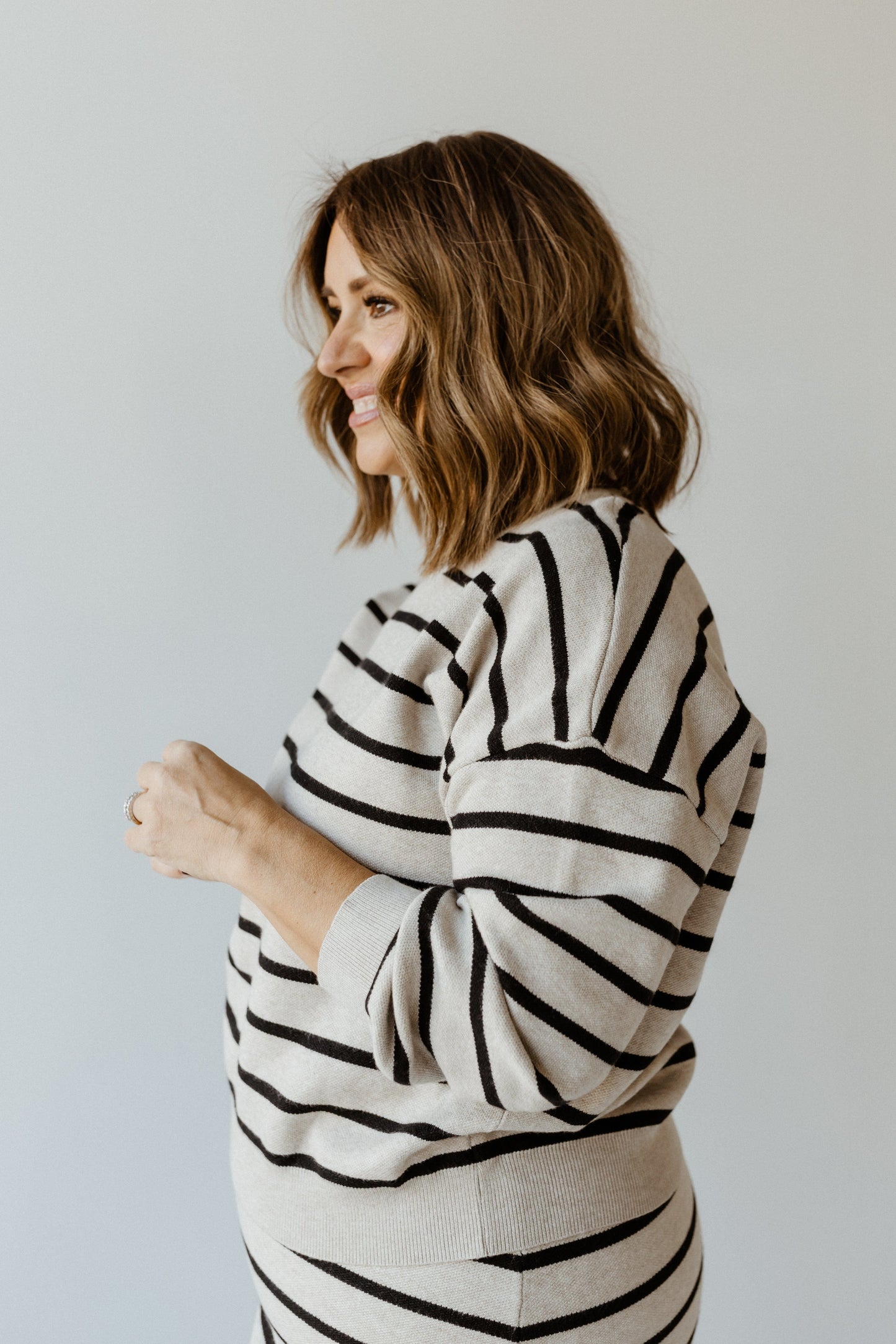 A person with shoulder-length hair models a knit striped sweater featuring dolman blouson sleeves, standing gracefully against a plain background.