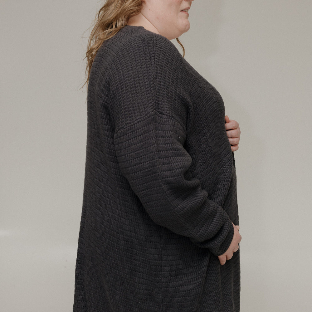 Woman wearing a dark gray cardigan against a plain background
