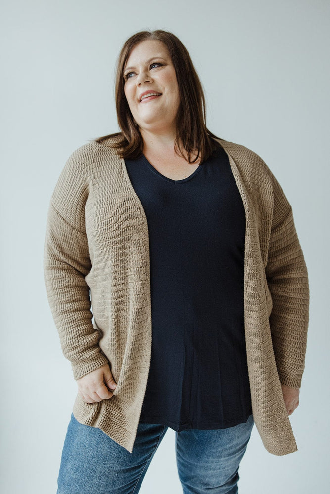 A person wearing the Yesta Knit Stripe Pattern Open Cardigan in Light Taupe and a black shirt smiles, standing against a light taupe background.