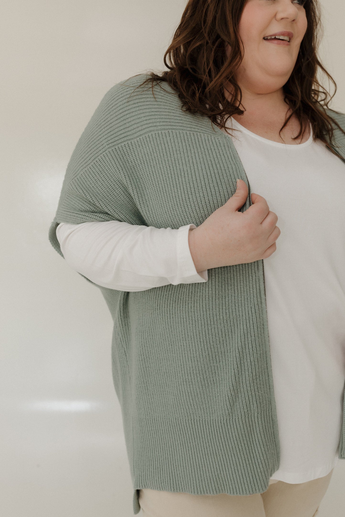 Person wearing a green ribbed sweater over a white shirt against a plain background