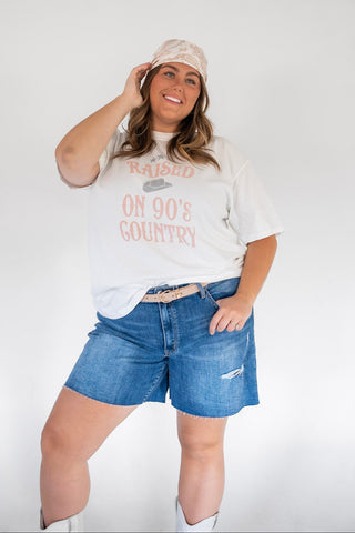 Woman wearing a graphic t-shirt, denim shorts, and a cap on a white background