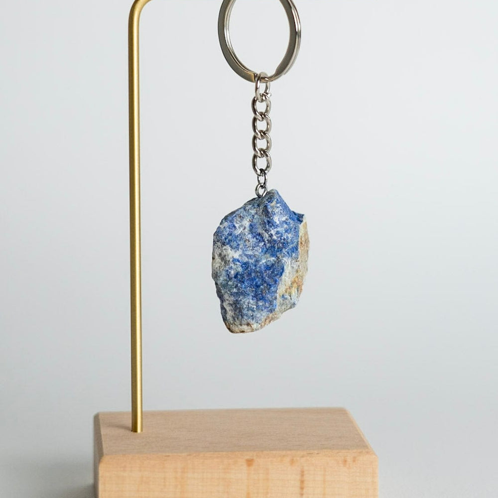 Keychain with a blue stone on a wooden stand against a light gray background
