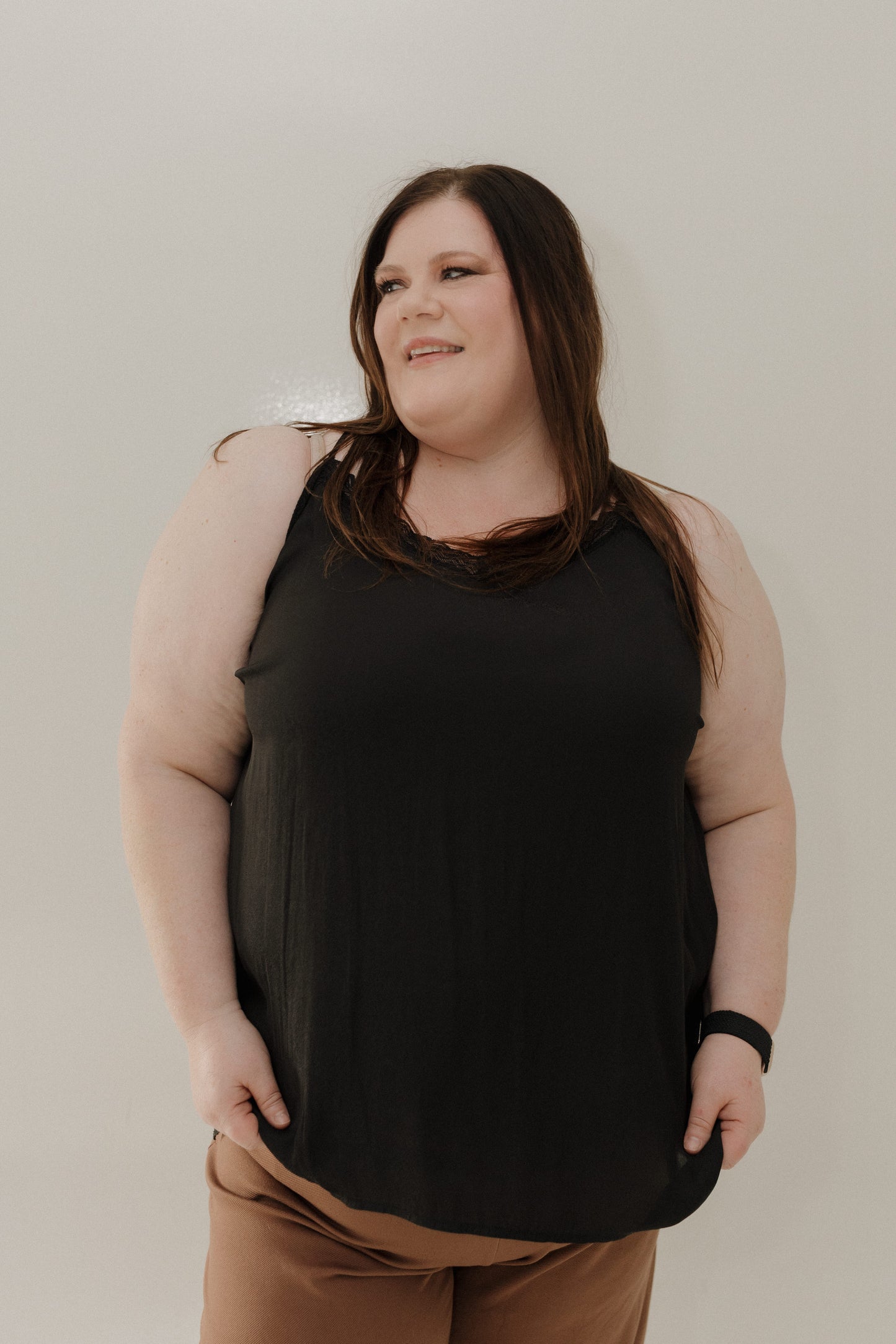 Woman wearing a black sleeveless top and brown pants against a plain background
