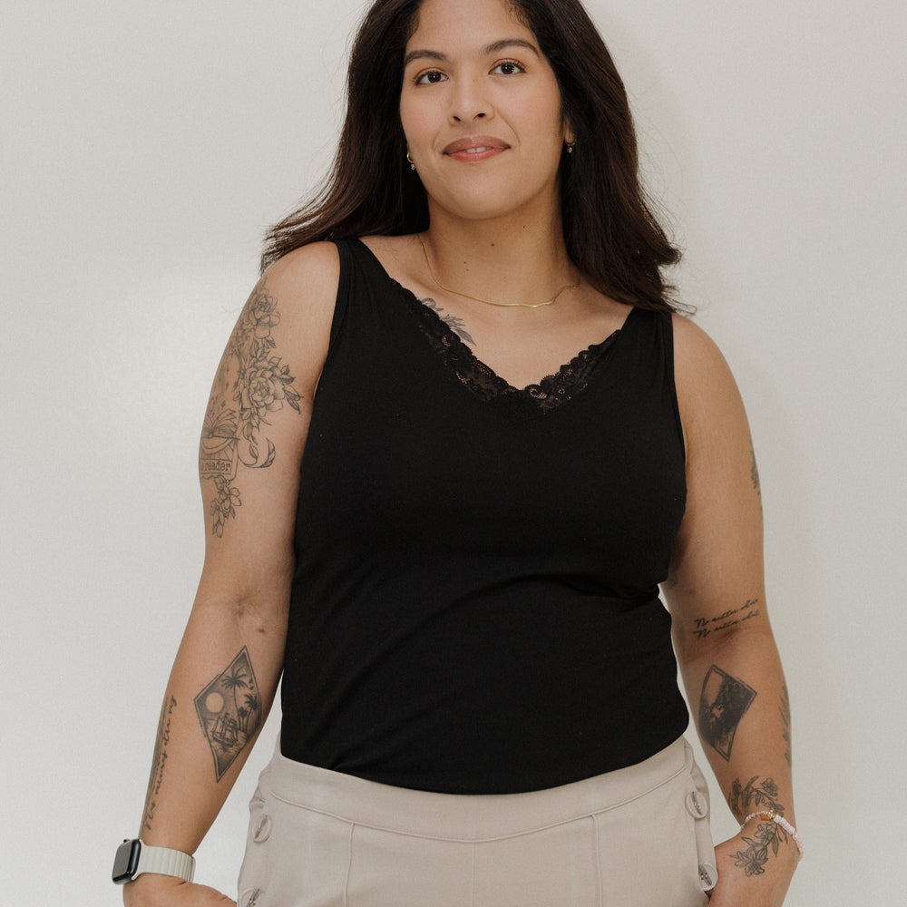 Woman wearing a black sleeveless top and beige pants against a plain background