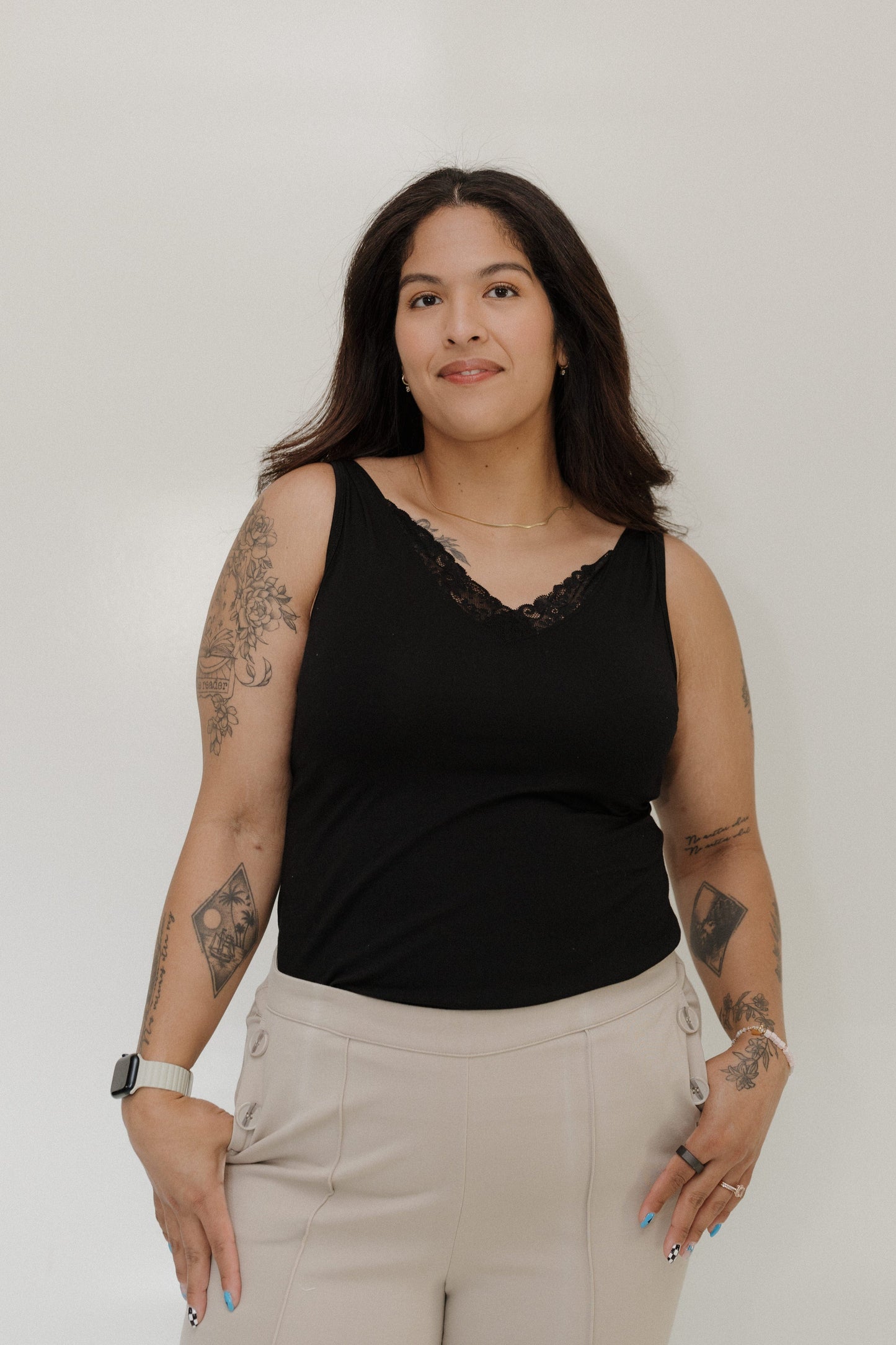 Woman wearing a black sleeveless top and beige pants against a plain background