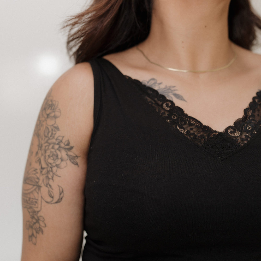 Person wearing a black sleeveless top with lace detailing on a plain background