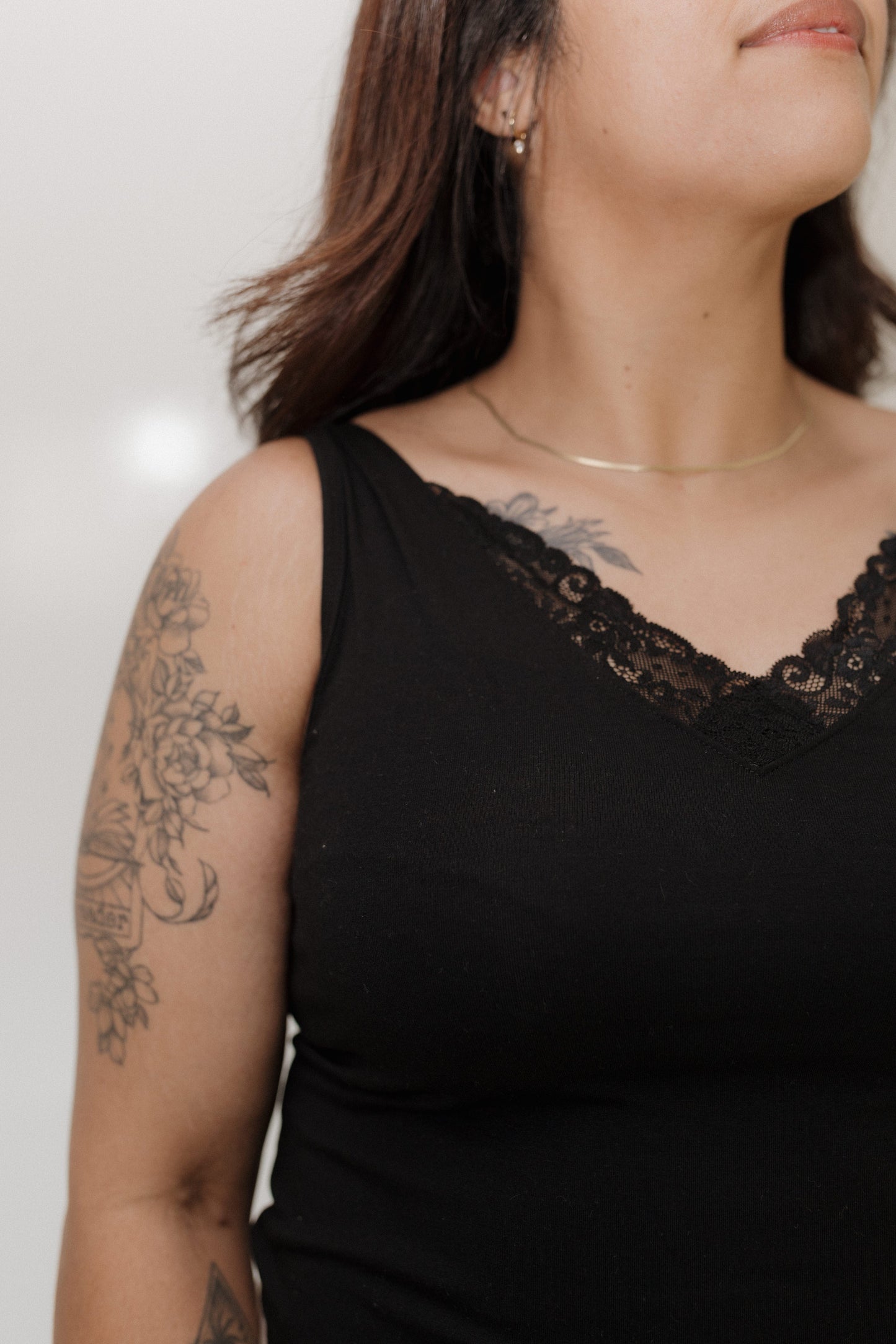 Person wearing a black sleeveless top with lace detailing on a plain background