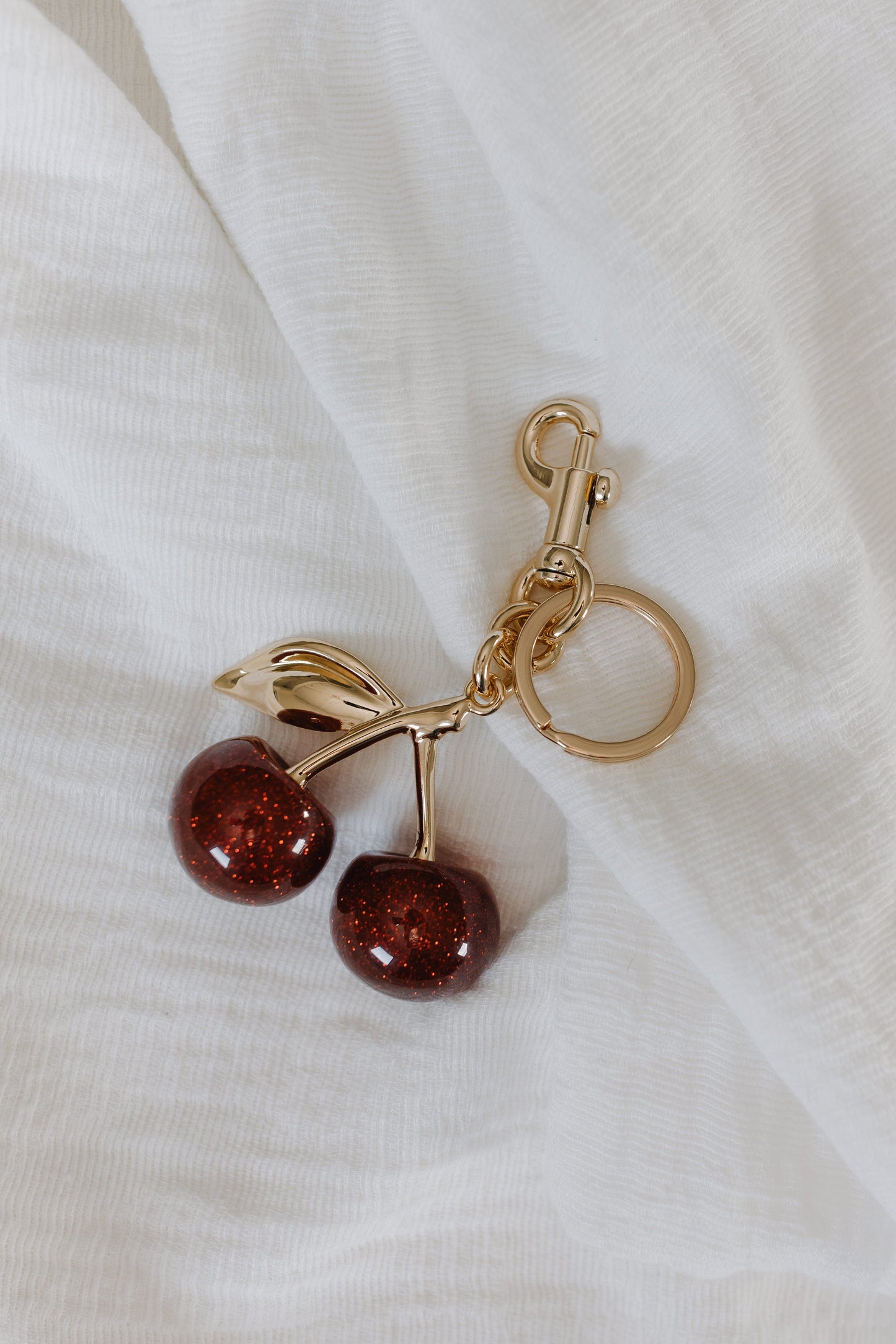 Gold keychain with cherries on a white fabric background