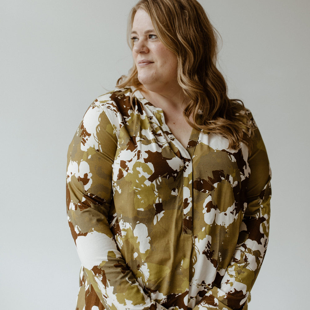 Against a plain background, a person with long hair is wearing the Yesta large abstract floral print blouse with banded hem and jeans, gazing to the side.