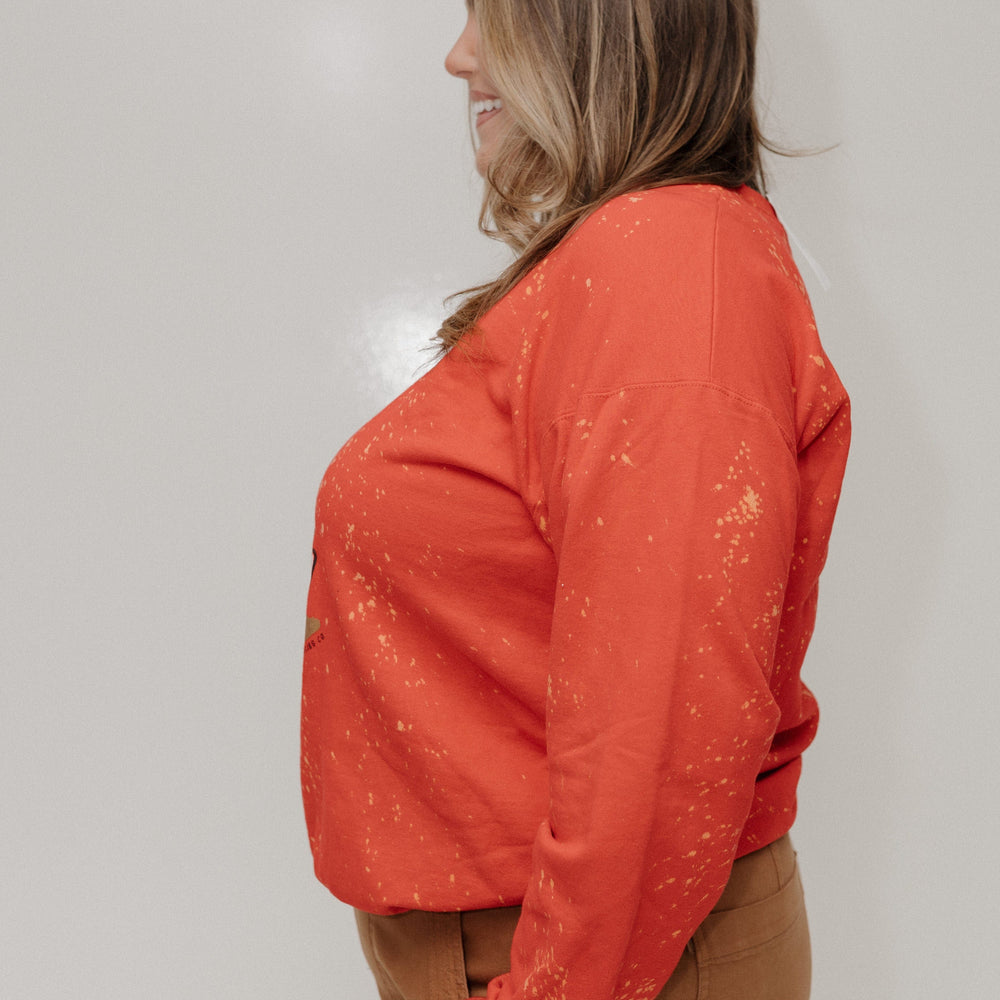 Woman wearing an orange long-sleeve top and brown pants against a white background