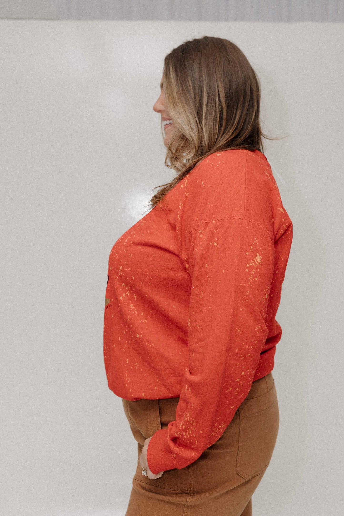 Woman wearing an orange long-sleeve top and brown pants against a white background