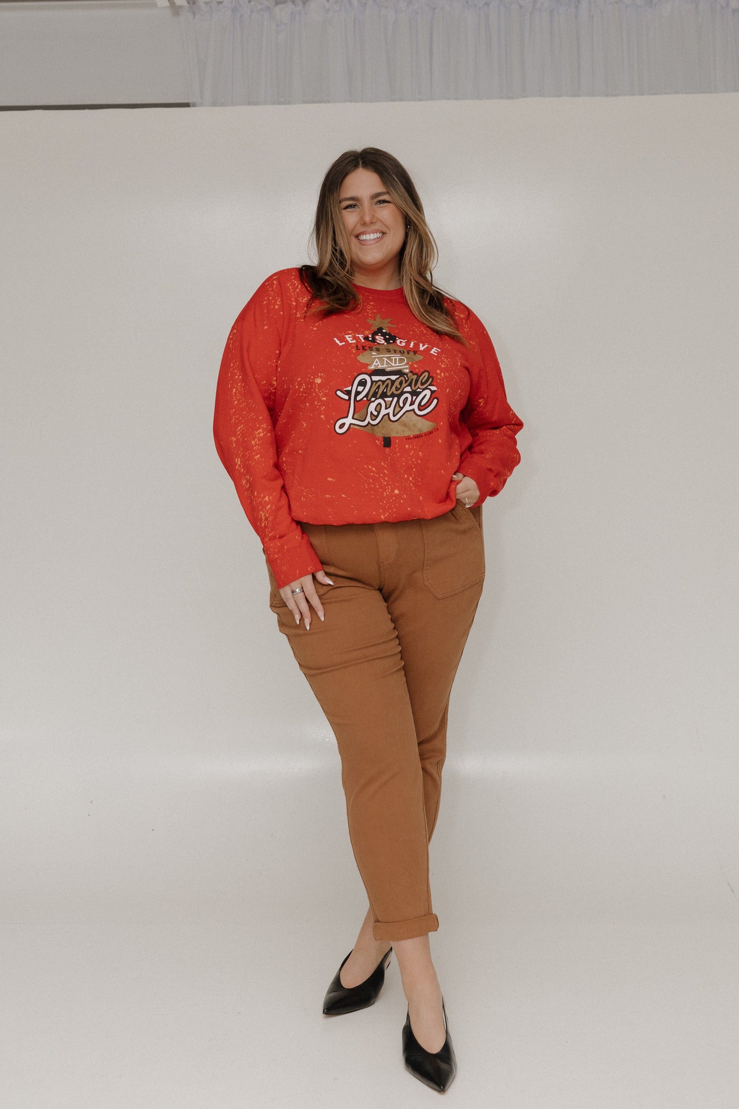 Woman wearing a red sweater with text and brown pants on a white background