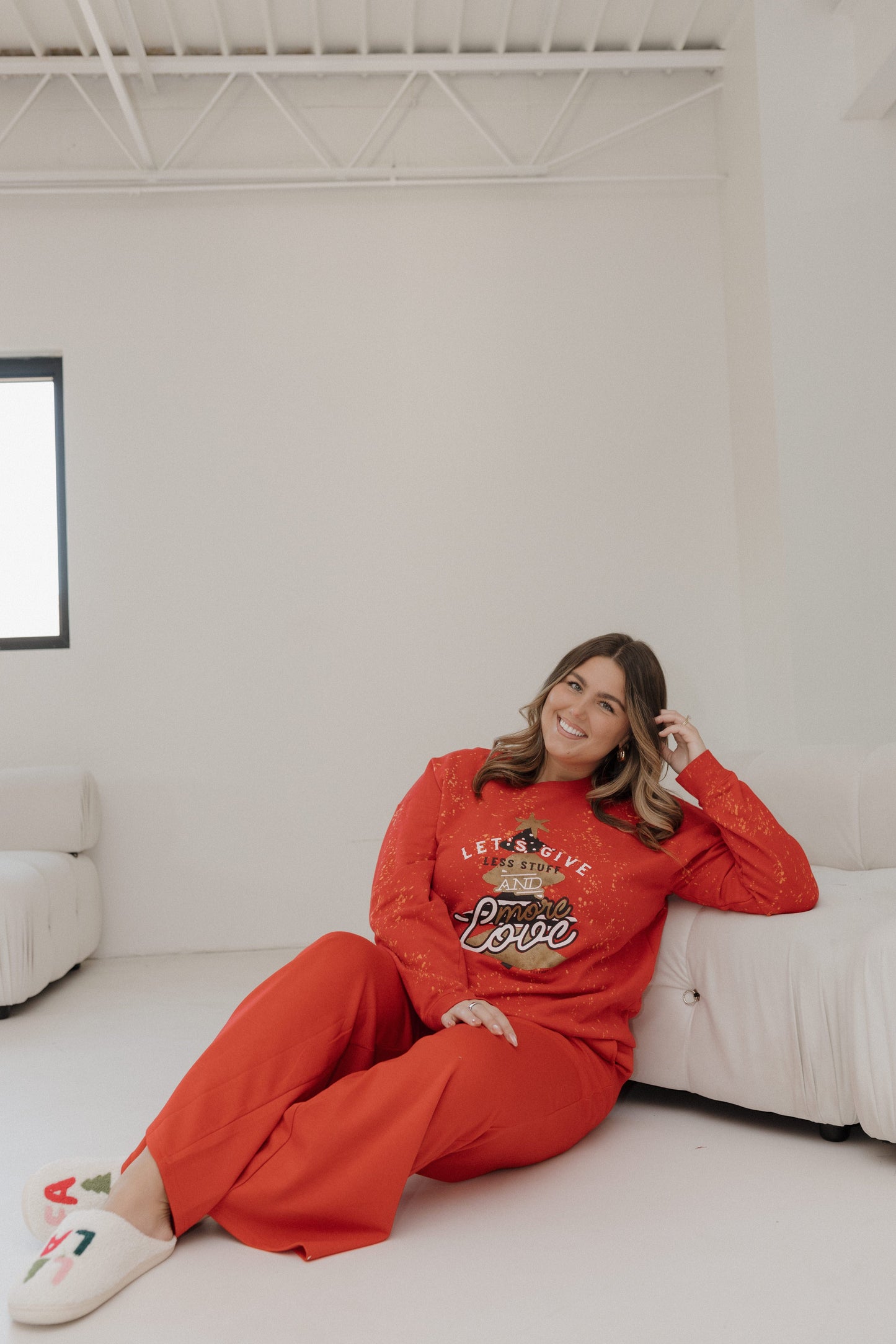 Woman in red outfit sitting on a white couch in a minimalistic room.