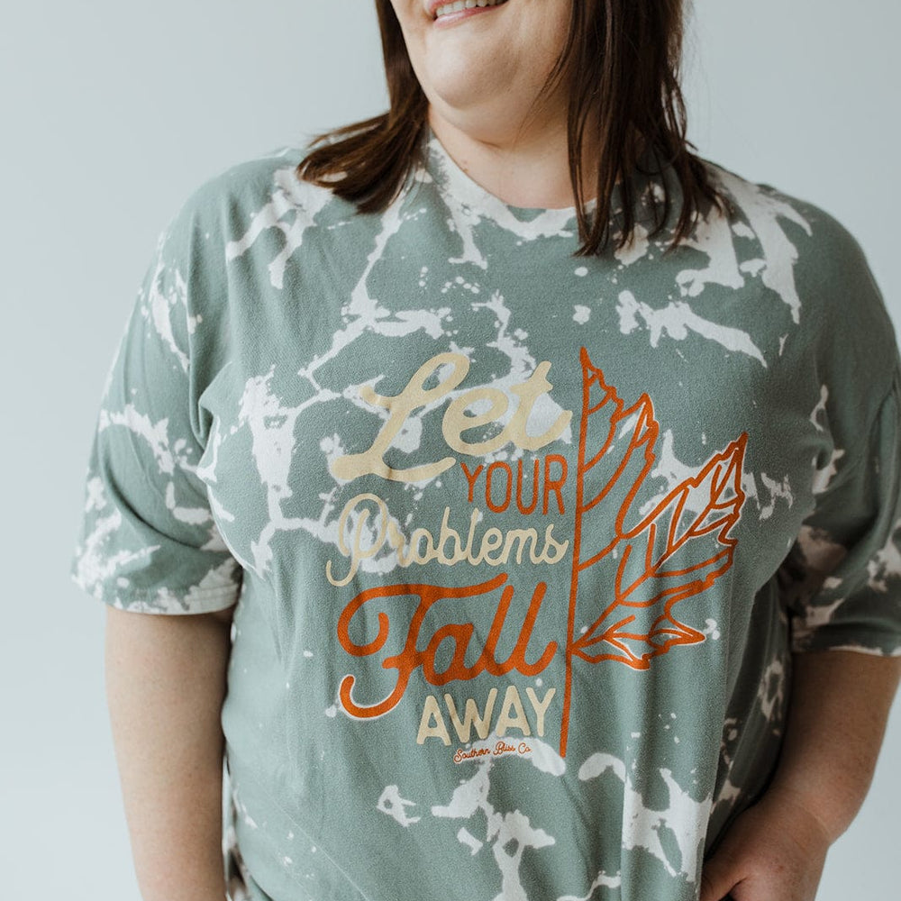 A person beams in the Love Marlow "LET YOUR PROBLEMS FALL AWAY" graphic tee, featuring a leaf design and an inspirational message, perfect for fall fashion.