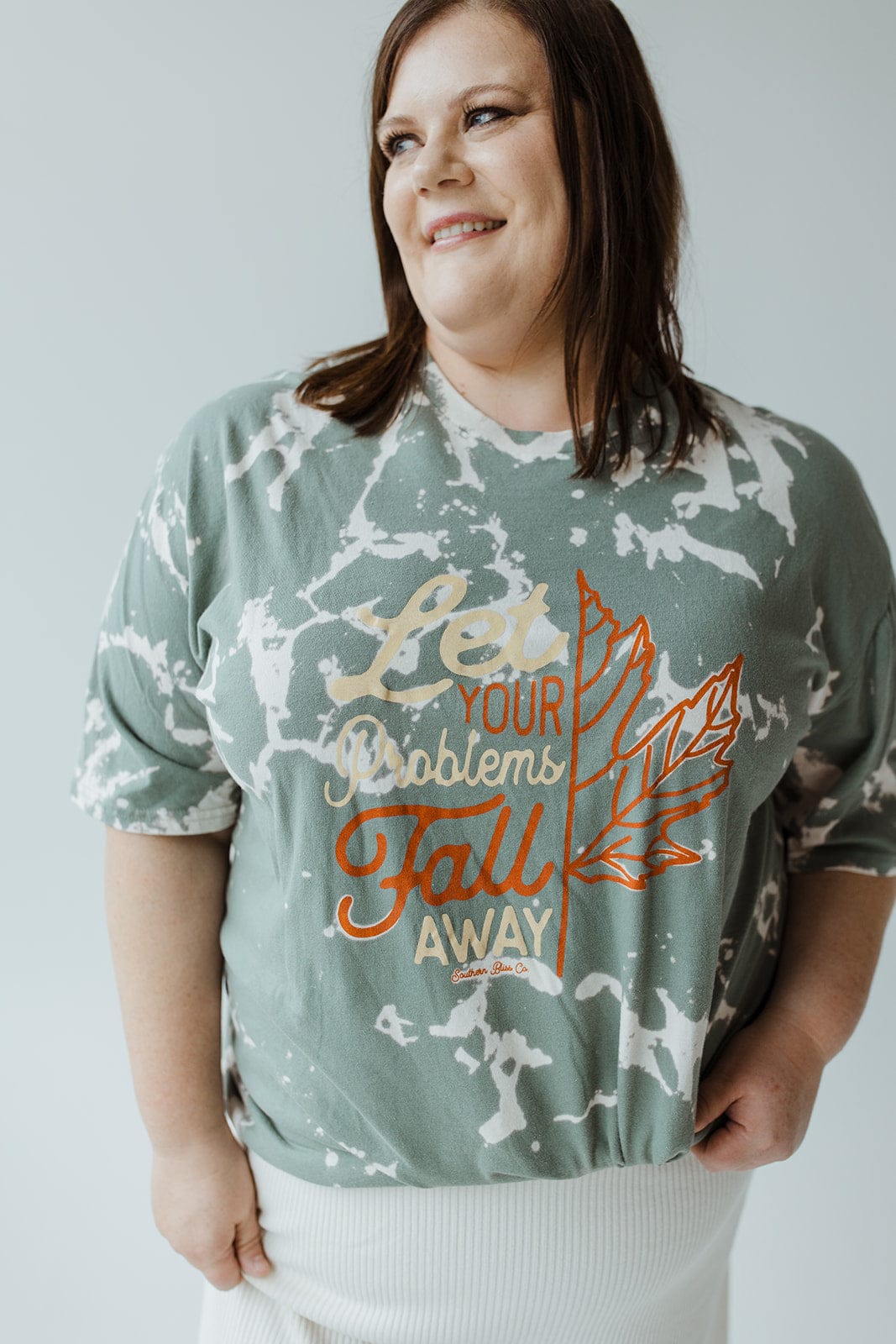 A person beams in the Love Marlow "LET YOUR PROBLEMS FALL AWAY" graphic tee, featuring a leaf design and an inspirational message, perfect for fall fashion.