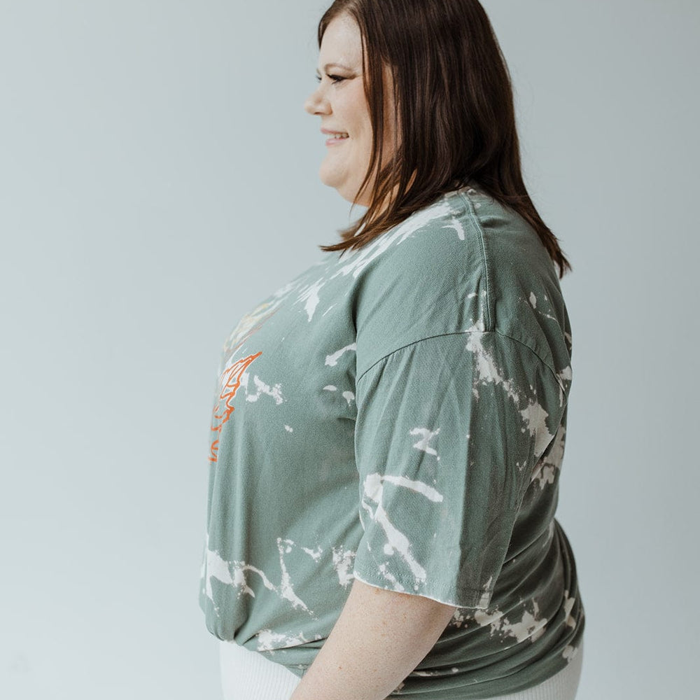 A person with brown hair is seen in profile against a plain background, donning the Love Marlow "LET YOUR PROBLEMS FALL AWAY" graphic tee with hand-bleached green tie-dye and white pants, capturing a unique fall fashion vibe.
