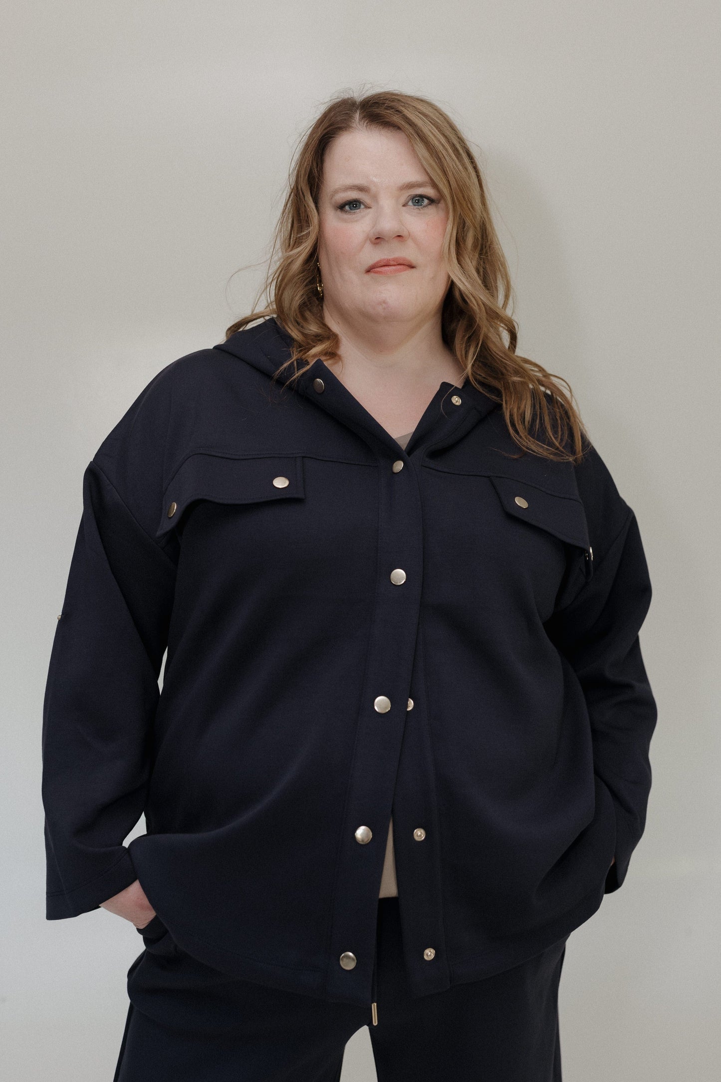 Person wearing a dark blue jacket with button details against a plain background