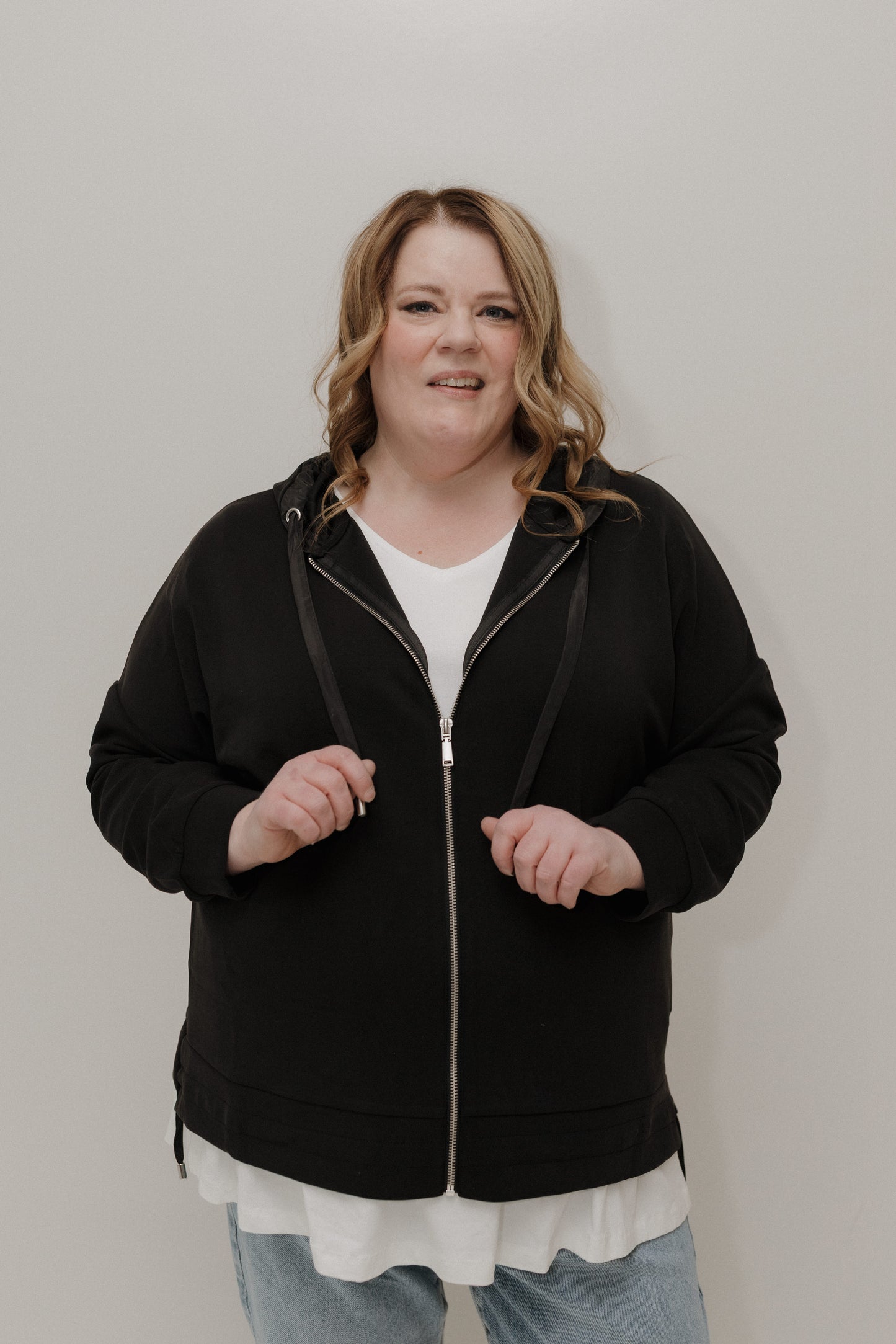 Person wearing a black zip-up hoodie against a plain background