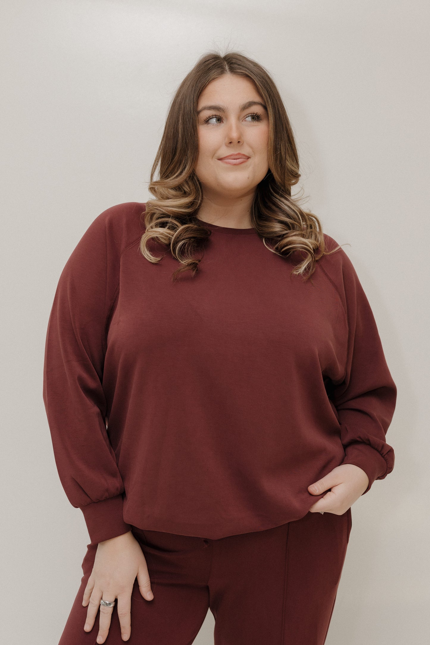 Woman wearing a maroon sweatshirt and pants against a plain background