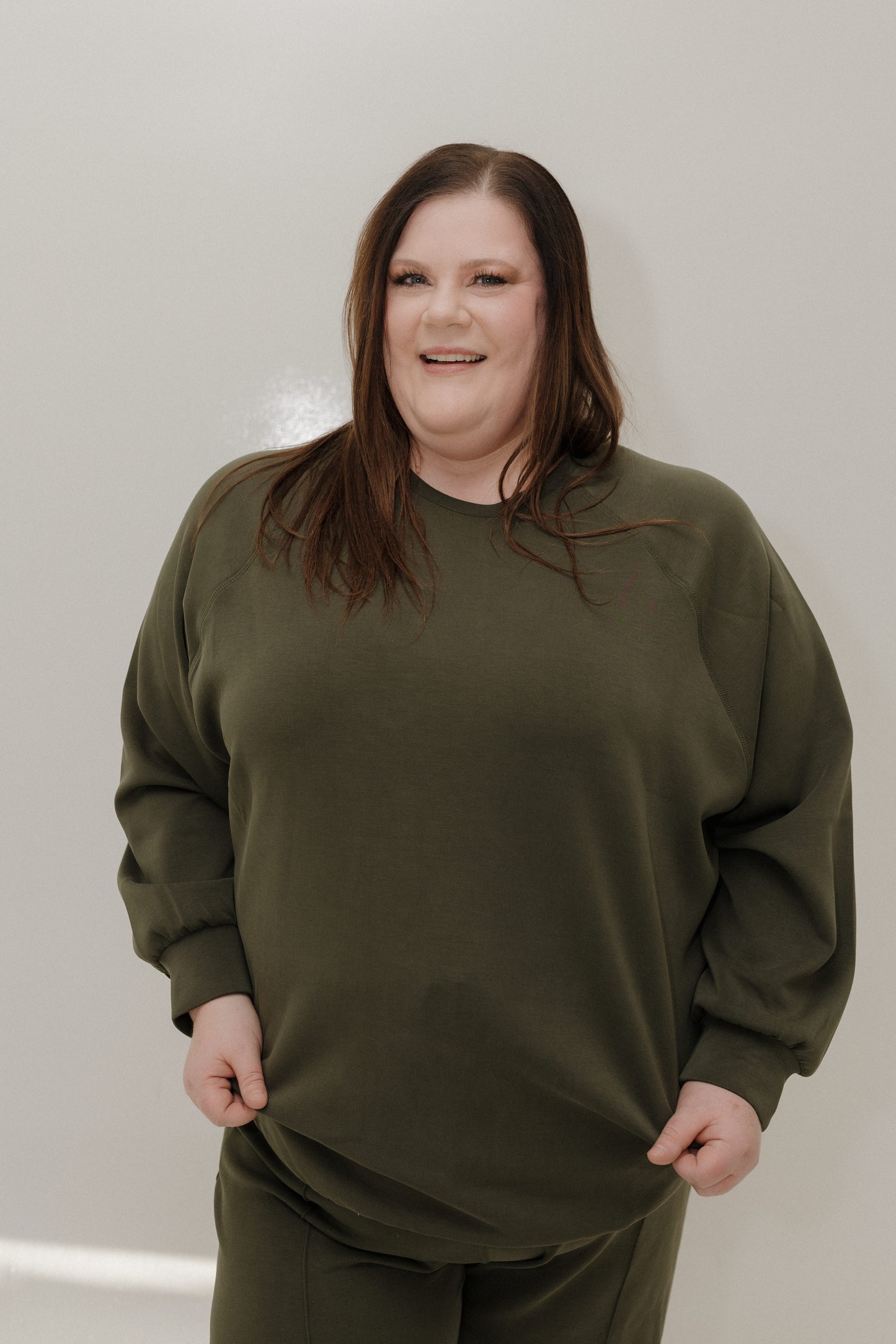 Person wearing an olive green sweatshirt and pants against a plain background