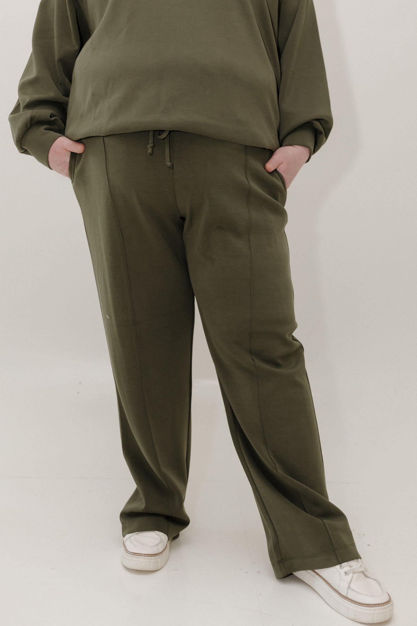 Person wearing olive green tracksuit with white shoes on a white background