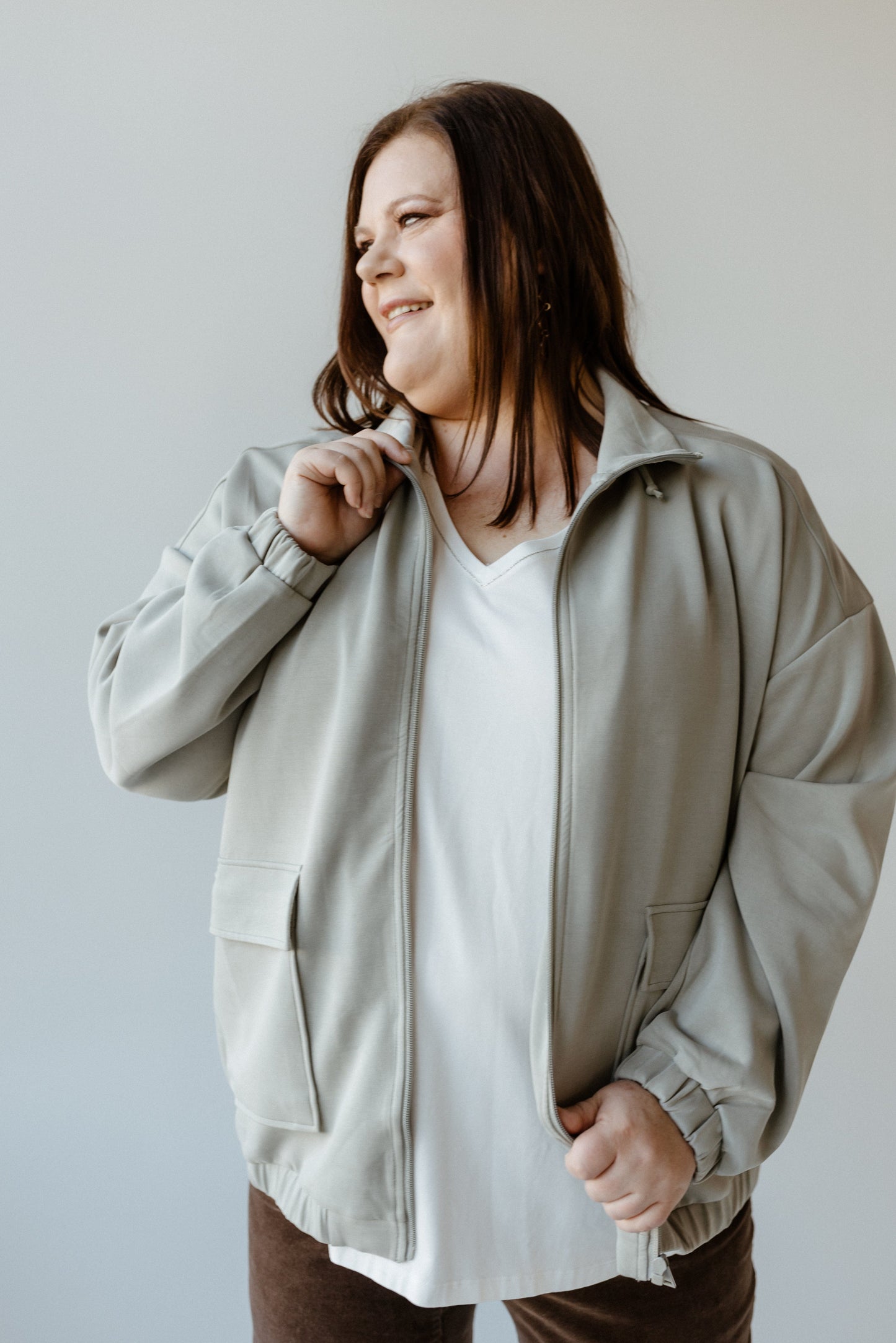 A person wearing a stylish urbanite jacket and white shirt smiles while looking to the side.