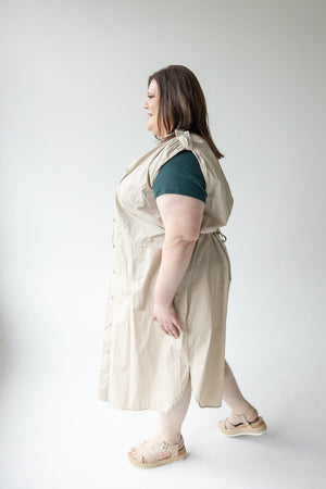 A person in a beige sleeveless dress and green shirt, versatile clothing at its best, stands sideways against a plain background wearing the LIGHTWEIGHT DUSTER VEST by Love Marlow.