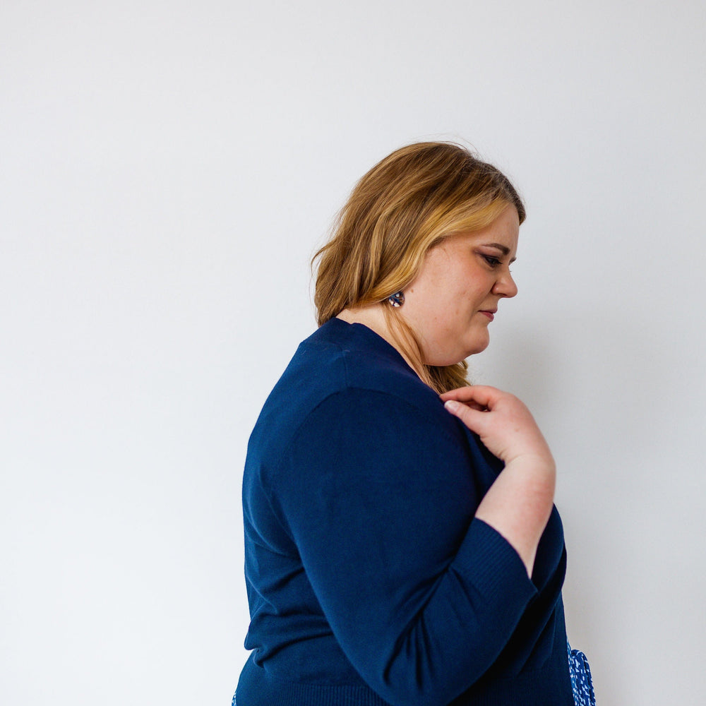 Person in a side profile wearing a navy blue top and patterned blue and white skirt, complemented by a lightweight navy cardigan with 3/4 length sleeves, against a white background.