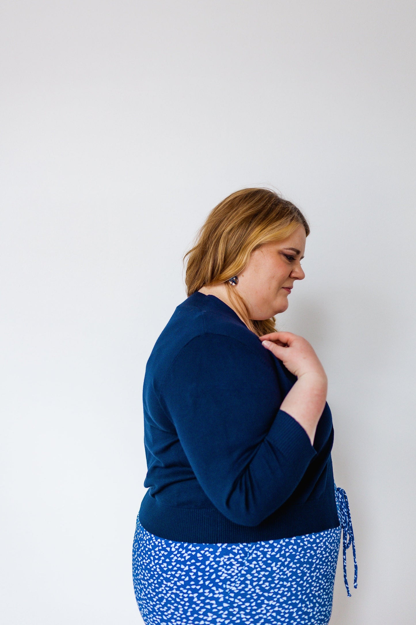 Person in a side profile wearing a navy blue top and patterned blue and white skirt, complemented by a lightweight navy cardigan with 3/4 length sleeves, against a white background.