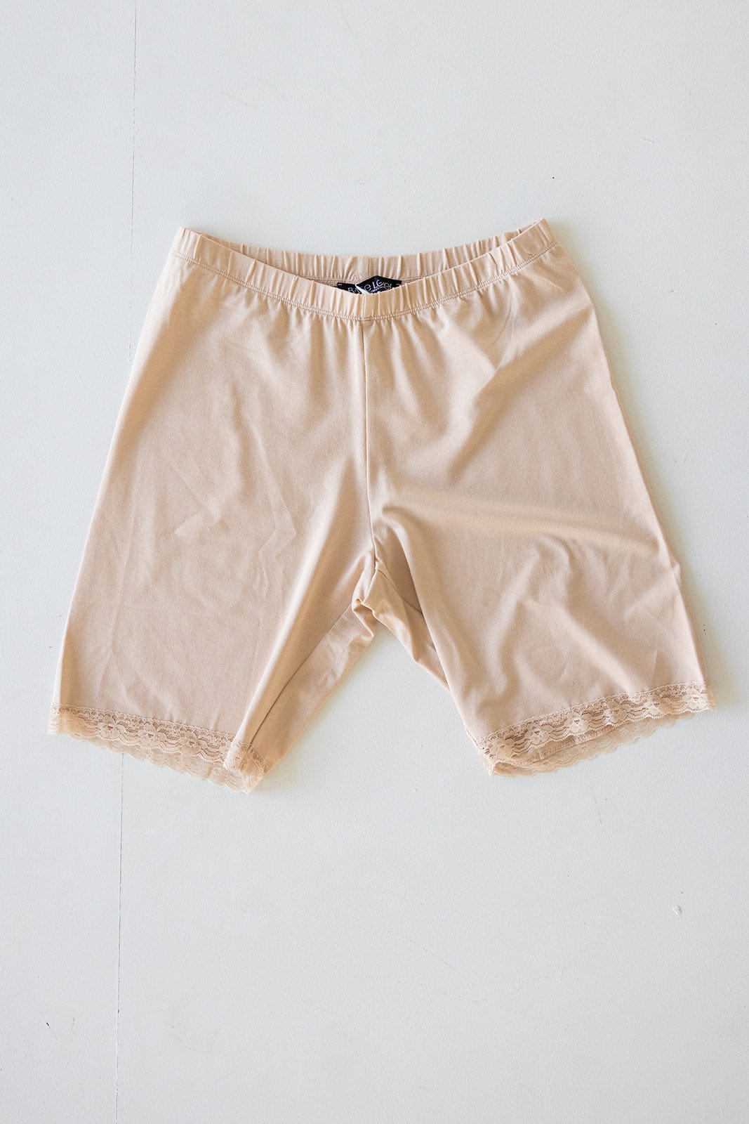 Beige shorts with lace trim on the hem, featuring a comfortable elastic waistband, laid flat against a white background.