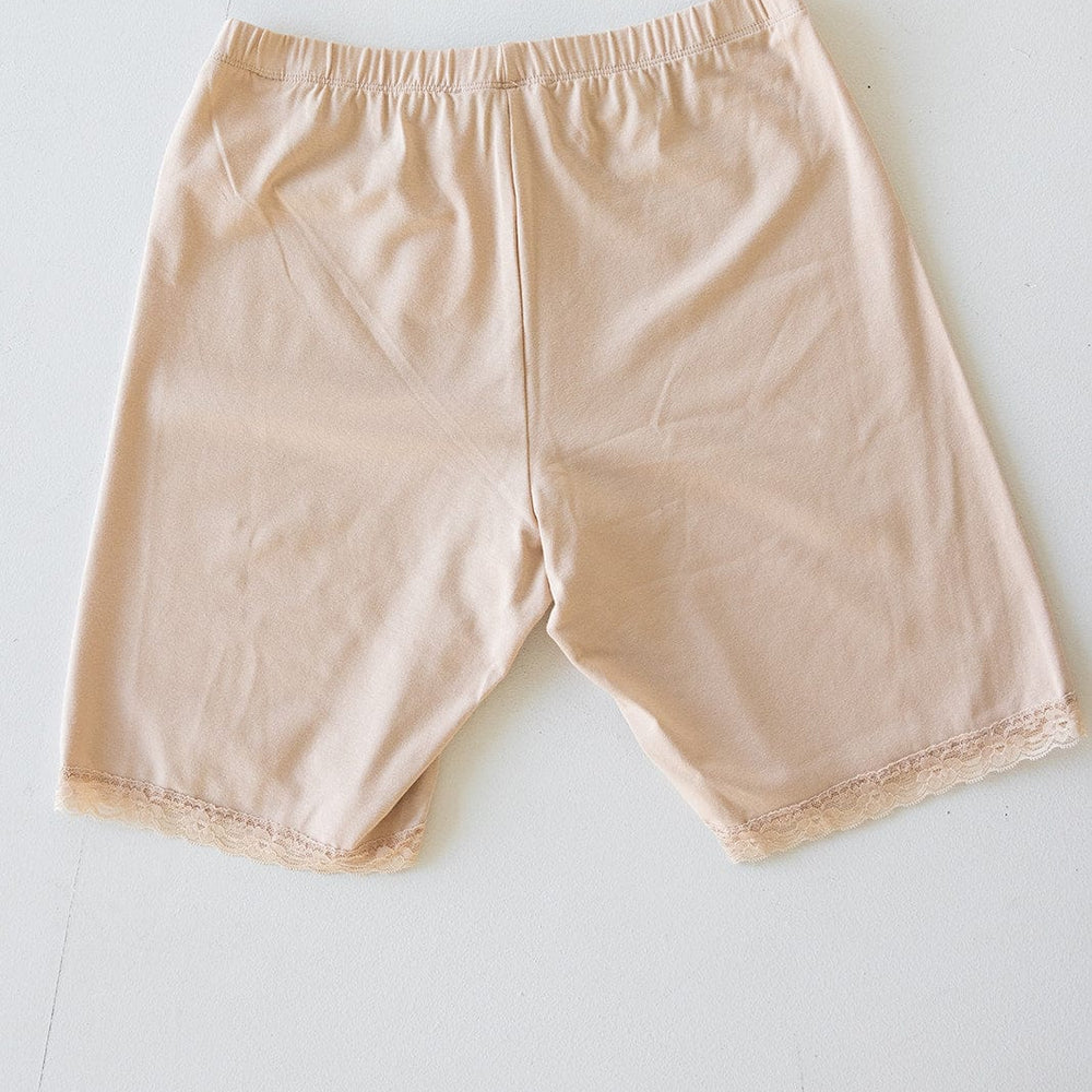 Beige undergarment shorts with a comfortable elastic waistband and lace trim on the legs, designed for thigh rub prevention, displayed flat on a white surface.