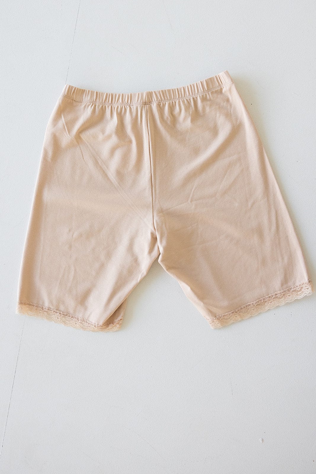 Beige undergarment shorts with a comfortable elastic waistband and lace trim on the legs, designed for thigh rub prevention, displayed flat on a white surface.