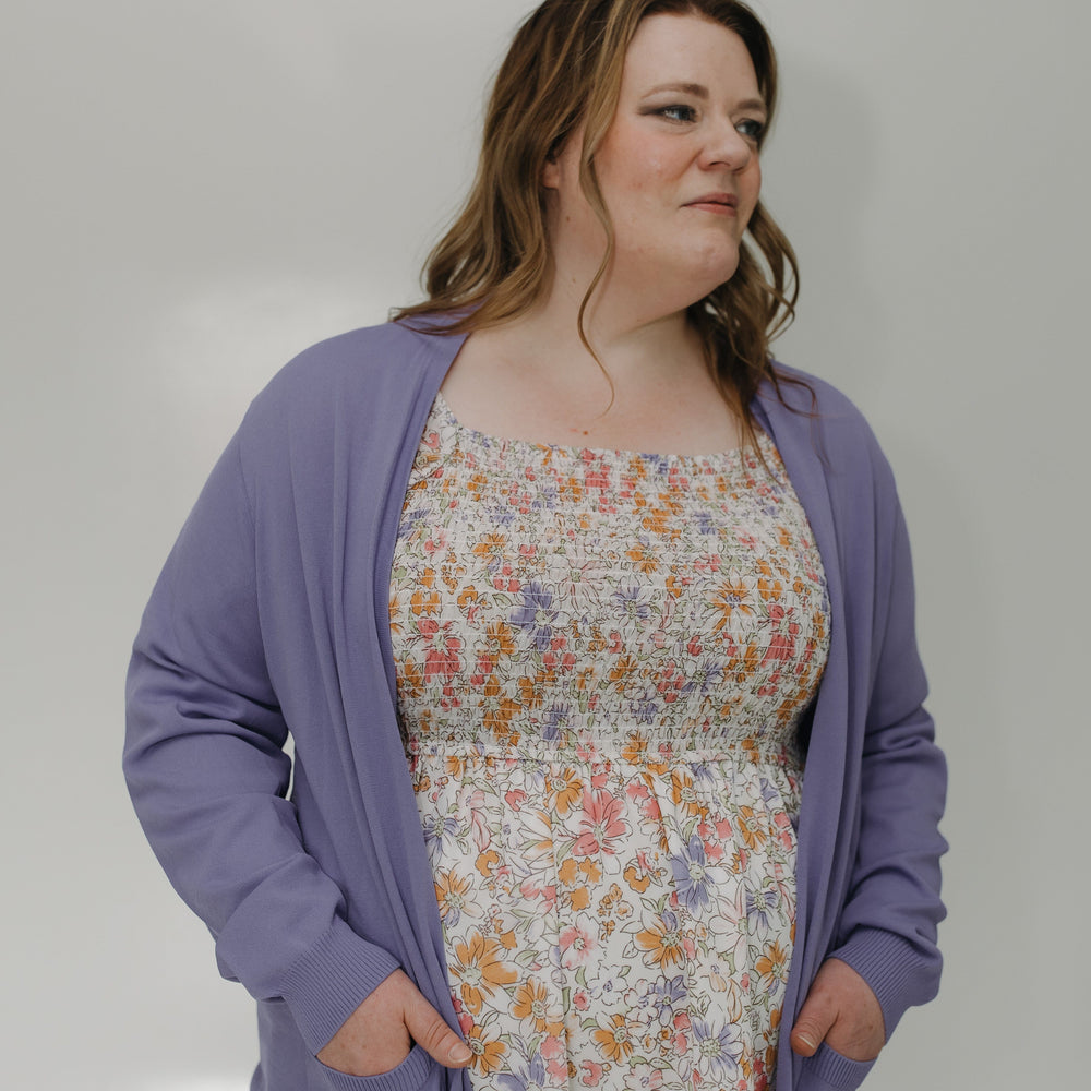 Woman wearing a floral dress with a purple cardigan against a plain background