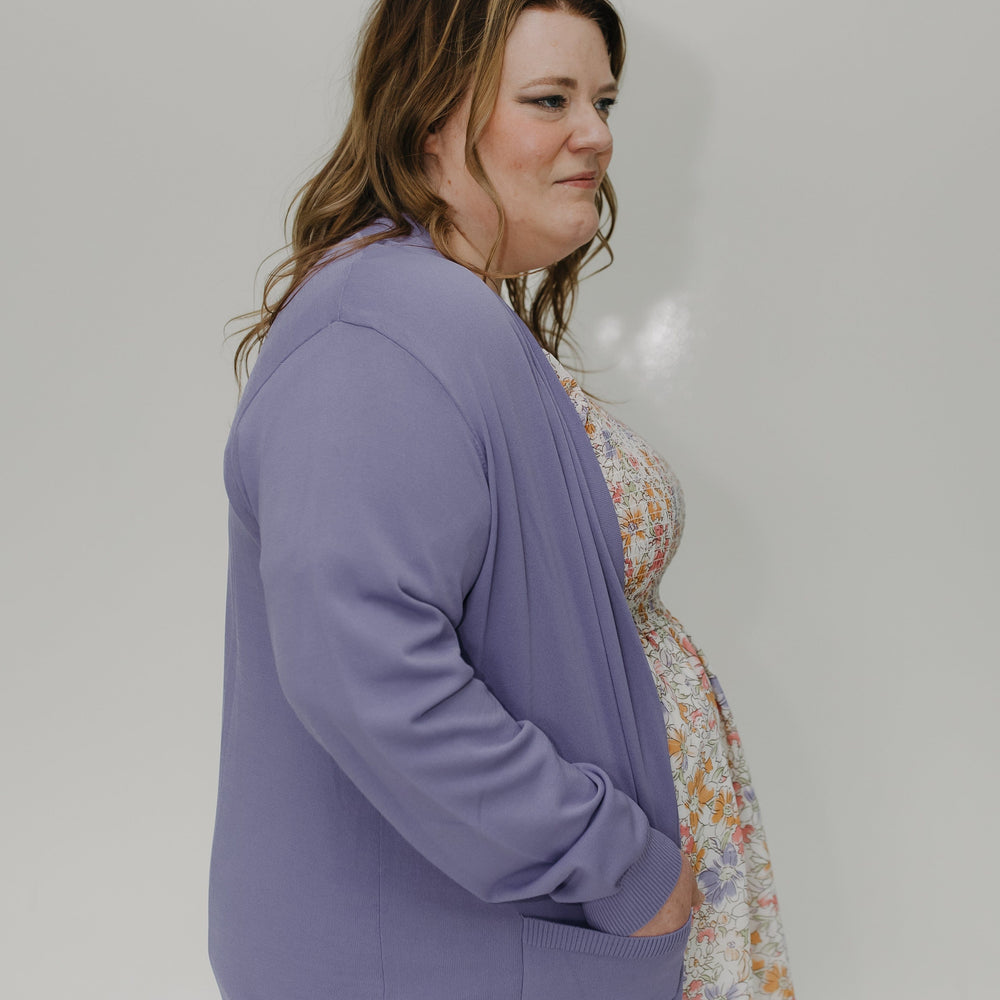 Woman wearing a purple cardigan over a floral dress against a plain background
