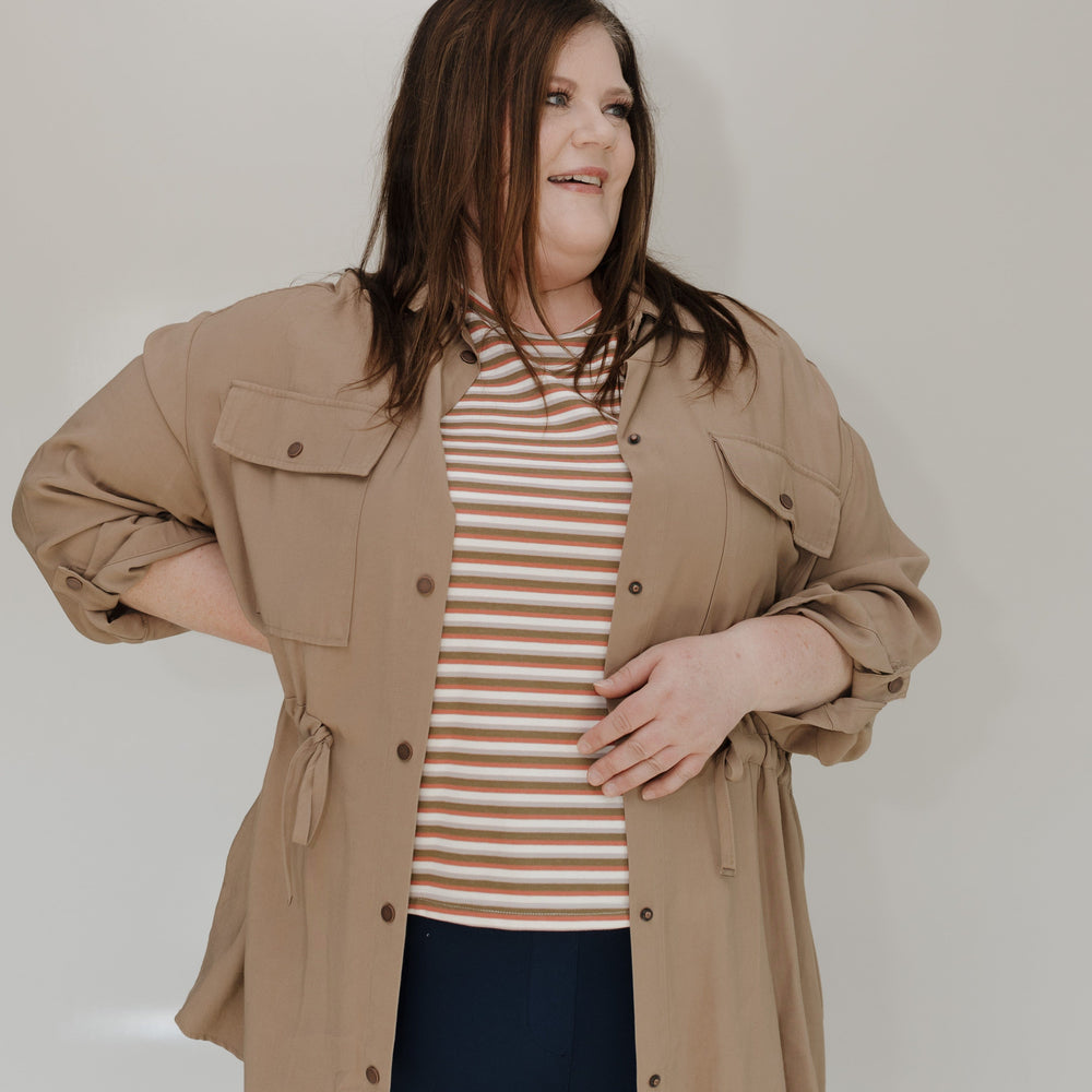 Woman wearing a beige jacket over a striped shirt against a plain background