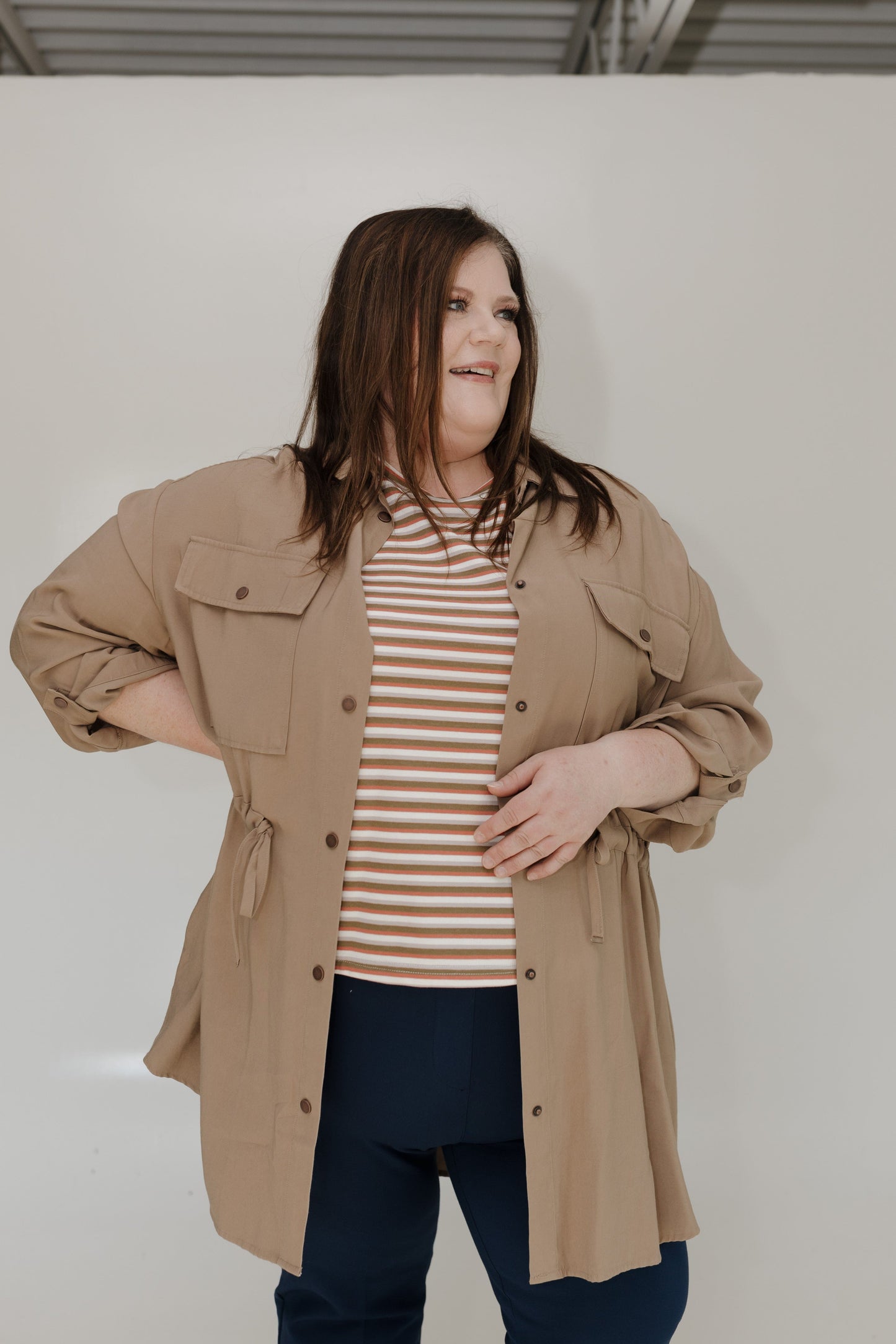 Woman wearing a beige jacket over a striped shirt against a plain background