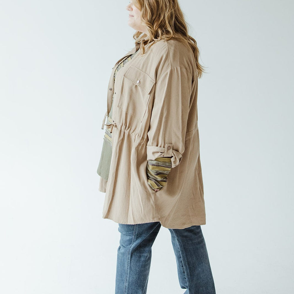 A person with long hair stands in profile wearing a beige shirt, tailored-fit blue jeans, sneakers, and a Yesta LIGHTWEIGHT CARGO JACKET.