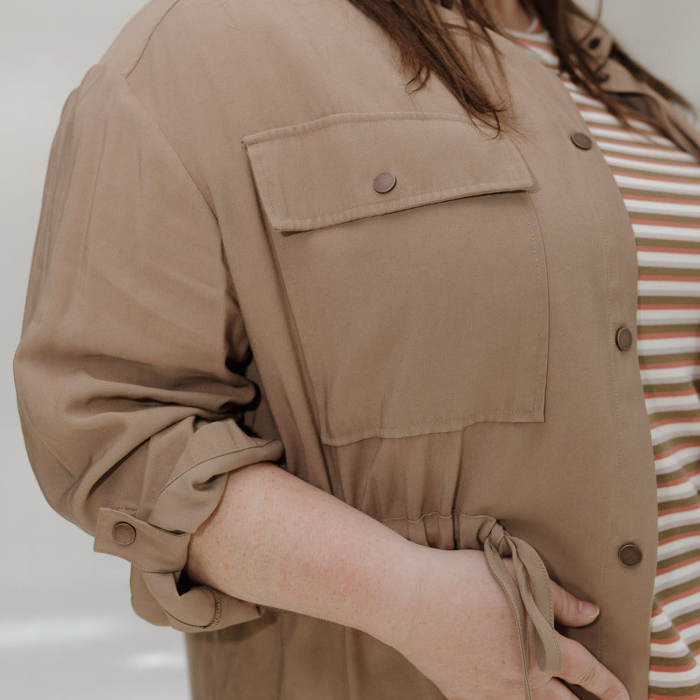 Person wearing a beige jacket over a striped shirt against a neutral background