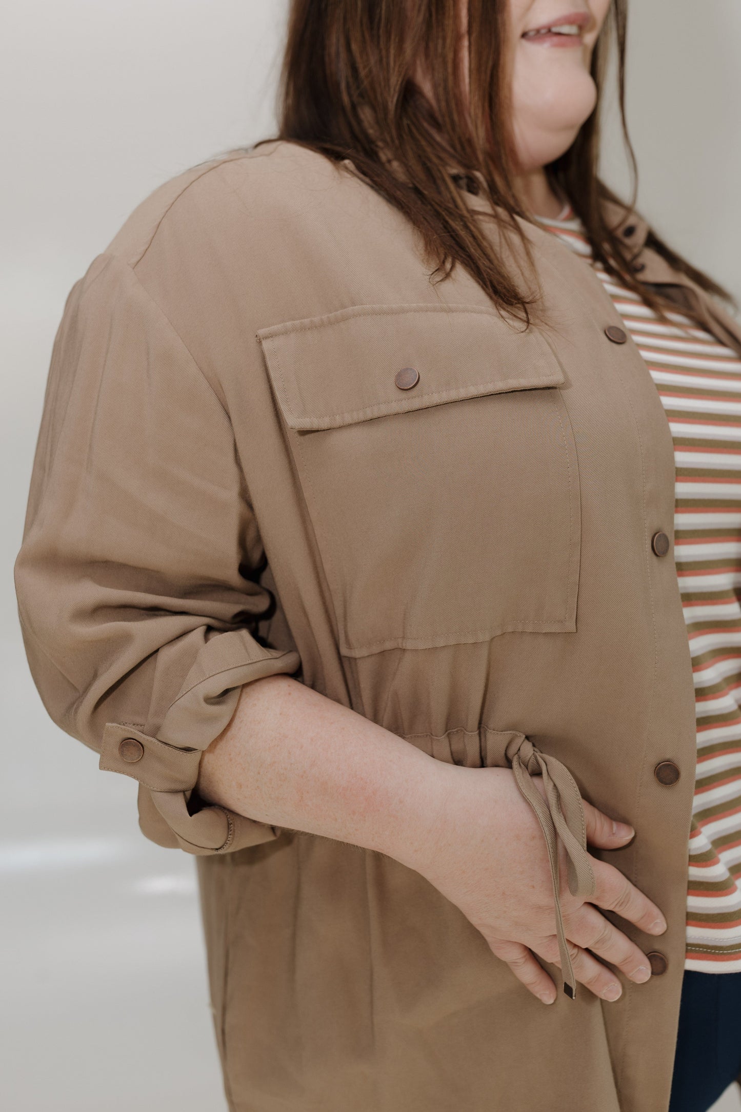 Person wearing a beige jacket over a striped shirt against a neutral background