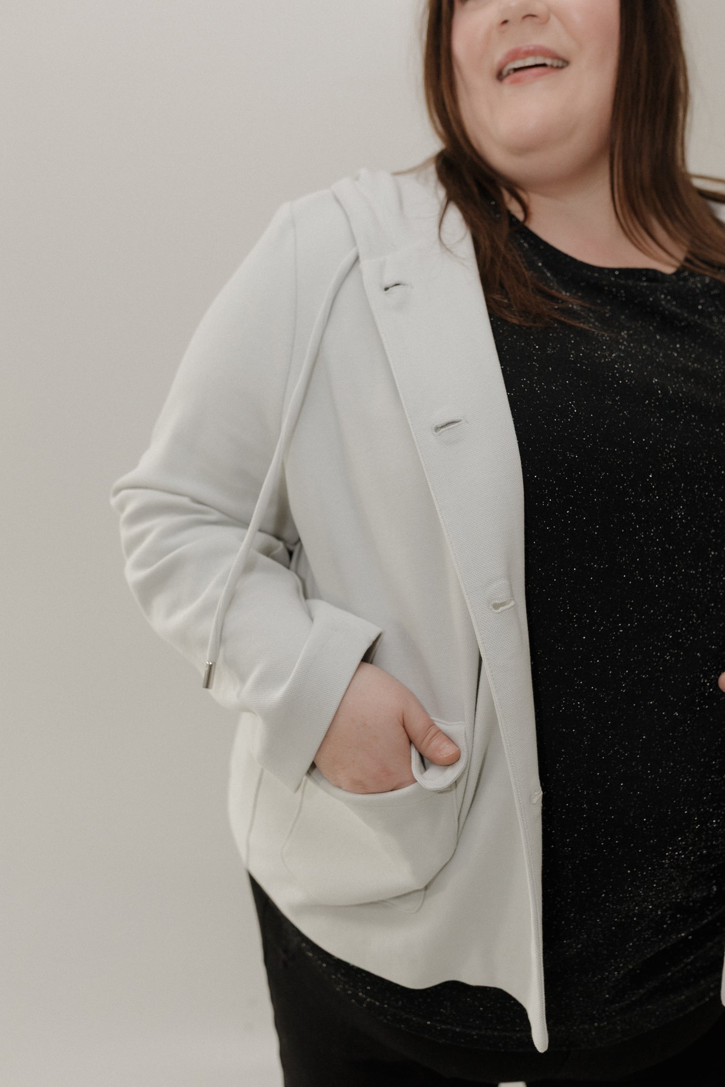 Person wearing a light gray blazer over a black top against a plain background