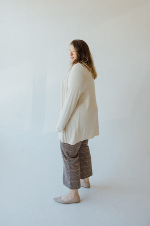 A person in a Yesta Lightweight Long-Sleeved Duster Cardigan in Sand and plaid pants stands on a light-colored floor against a plain background, looking to the side.