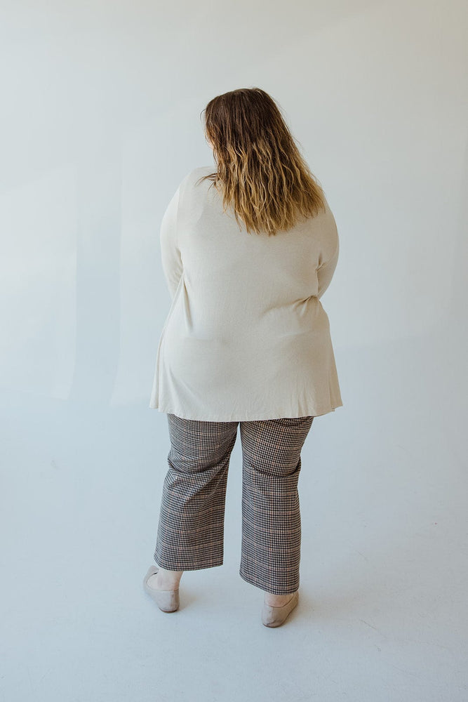 Person with long hair, wearing a Yesta Lightweight Long-Sleeved Duster Cardigan in Sand and checkered pants, is standing and facing away from the camera against a plain background.